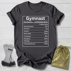 Black t-shirt with 'Gymnast' nutrition facts graphic on a wooden surface with socks and a drawstring bag.
