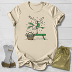 Beige t-shirt with a graphic design of a rabbit on a bench with an Easter basket, socks, and a drawstring bag on a light wooden surface.