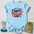 Light blue -shirt with 'Coach's Favorite' text on a light wooden surface with socks and a drawstring bag.