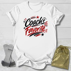 White t-shirt with 'Coach's Favorite' text on a light wooden surface with socks and a drawstring bag.