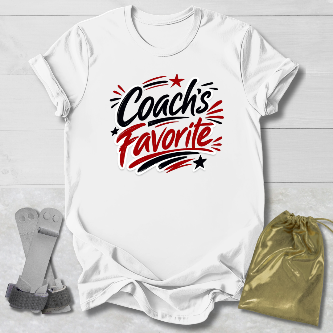 White t-shirt with 'Coach's Favorite' text on a light wooden surface with socks and a drawstring bag.