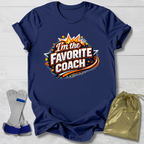 Navy blue t-shirt with 'I'm the Favorite Coach' design on a light wooden surface.