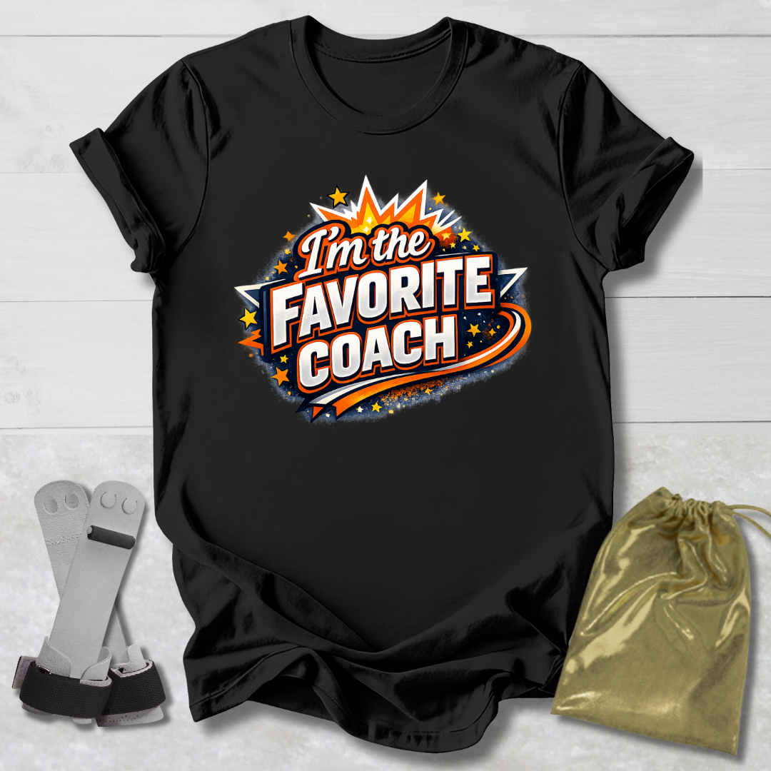 Black t-shirt with 'I'm the Favorite Coach' design on a light wooden surface with socks and a drawstring bag.