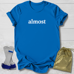Blue t-shirt with 'almost' text, socks, and a drawstring bag on a light wooden surface.