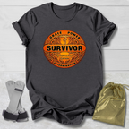 Gray t-shirt with orange and black Survivor Gymnast Edition graphic design on a light wooden surface.
