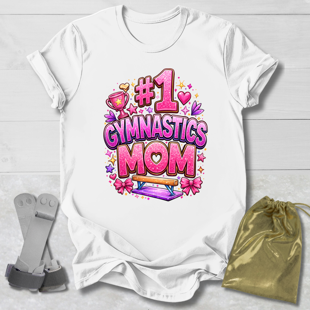 White t-shirt with '#1 Gymnastics Mom' design on a light wooden surface with socks and a drawstring bag.