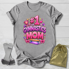Gray t-shirt with '#1 Gymnastics Mom' design on a light wooden surface with socks and a drawstring bag.