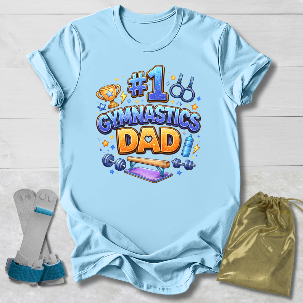 Light blue t-shirt with '#1 Gymnastics Dad' design on a wooden surface with socks and a drawstring bag.