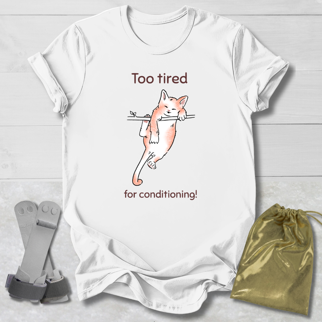 White t-shirt with a cat illustration and a cat that's too tired for gymnastics conditioning text, paired with socks and a drawstring bag on a light wooden surface.