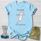 Light blue t-shirt with a cat that's too tired for gymnastics conditioning graphic and text, displayed with socks and a drawstring bag on a light wooden surface.