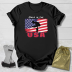 Black t-shirt with Gymnast American flag graphic and text 'Made in the USA' on a wooden surface.