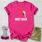 Pink t-shirt with a graphic and 'MEET WEEK' text, paired with socks and a drawstring bag on a light wooden surface.