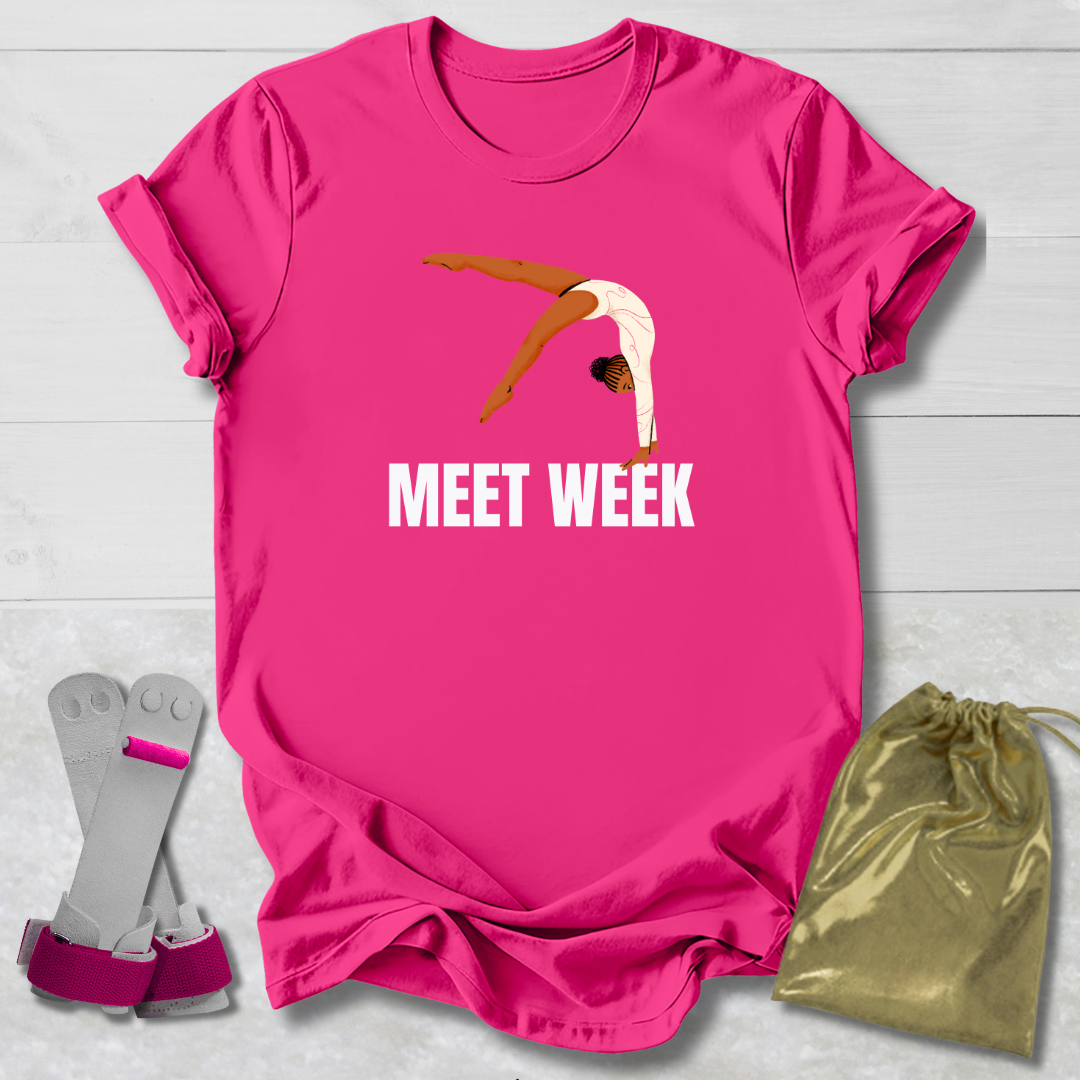 Pink t-shirt with a graphic and 'MEET WEEK' text, paired with socks and a drawstring bag on a light wooden surface.