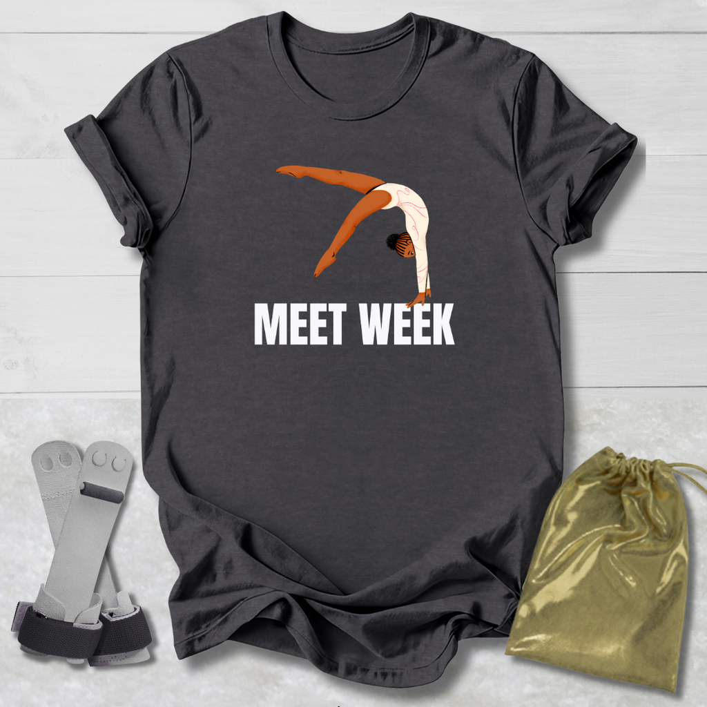 Dark gray t-shirt with a graphic of a diver and 'MEET WEEK' text, placed on a light wooden surface with socks and a drawstring bag.