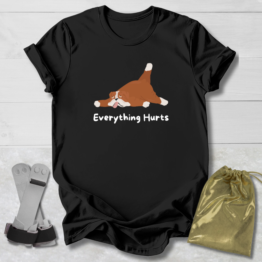 Black t-shirt with a cartoon dog and 'Everything Hurts' text, displayed on a light wooden surface with socks and a drawstring bag.