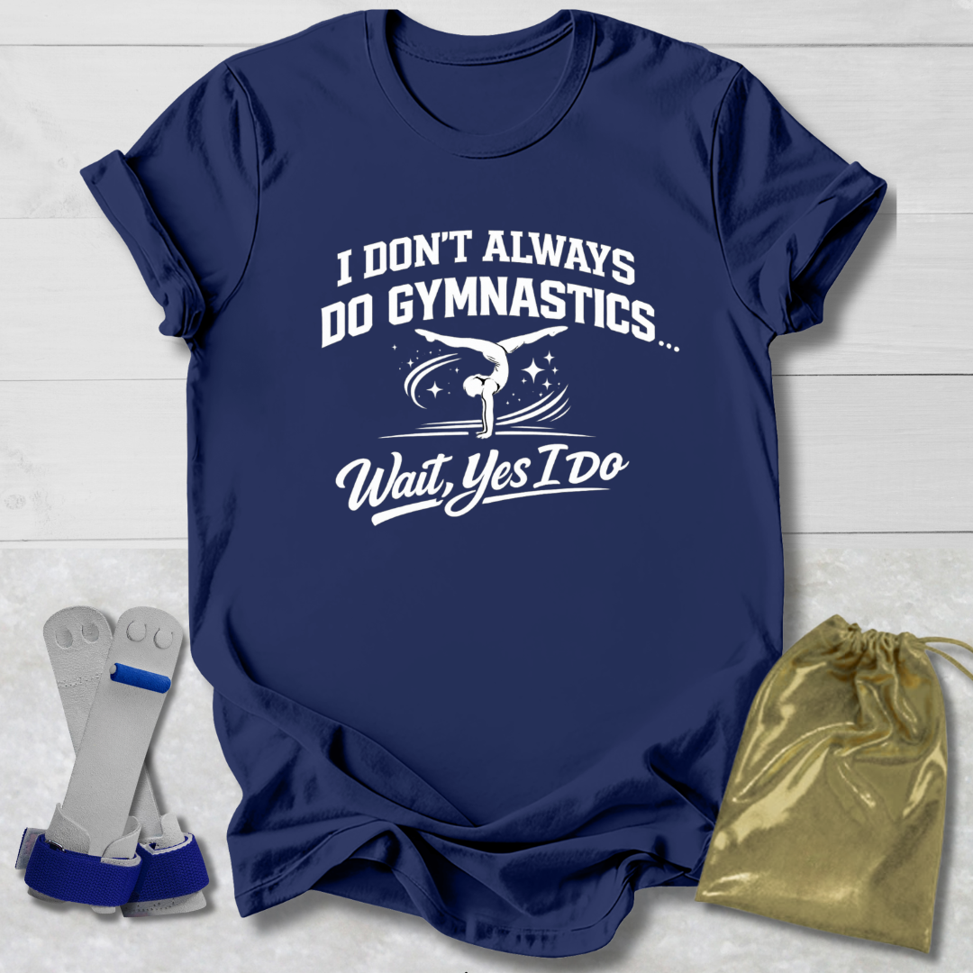 Navy blue t-shirt with white I don't always do gymnastics . . . wait, yes I do text and graphics on a light wooden surface, accompanied by gray socks and a gold drawstring bag.