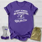Purple t-shirt with white I don't always do gymnastics . . . wait, yes I do text and graphics on a light wooden surface, accompanied by gray socks and a gold drawstring bag.