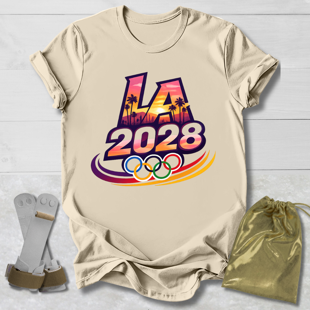 Beige t-shirt with 'LA 2028' Olympic design on a light wooden surface with socks and a drawstring bag.