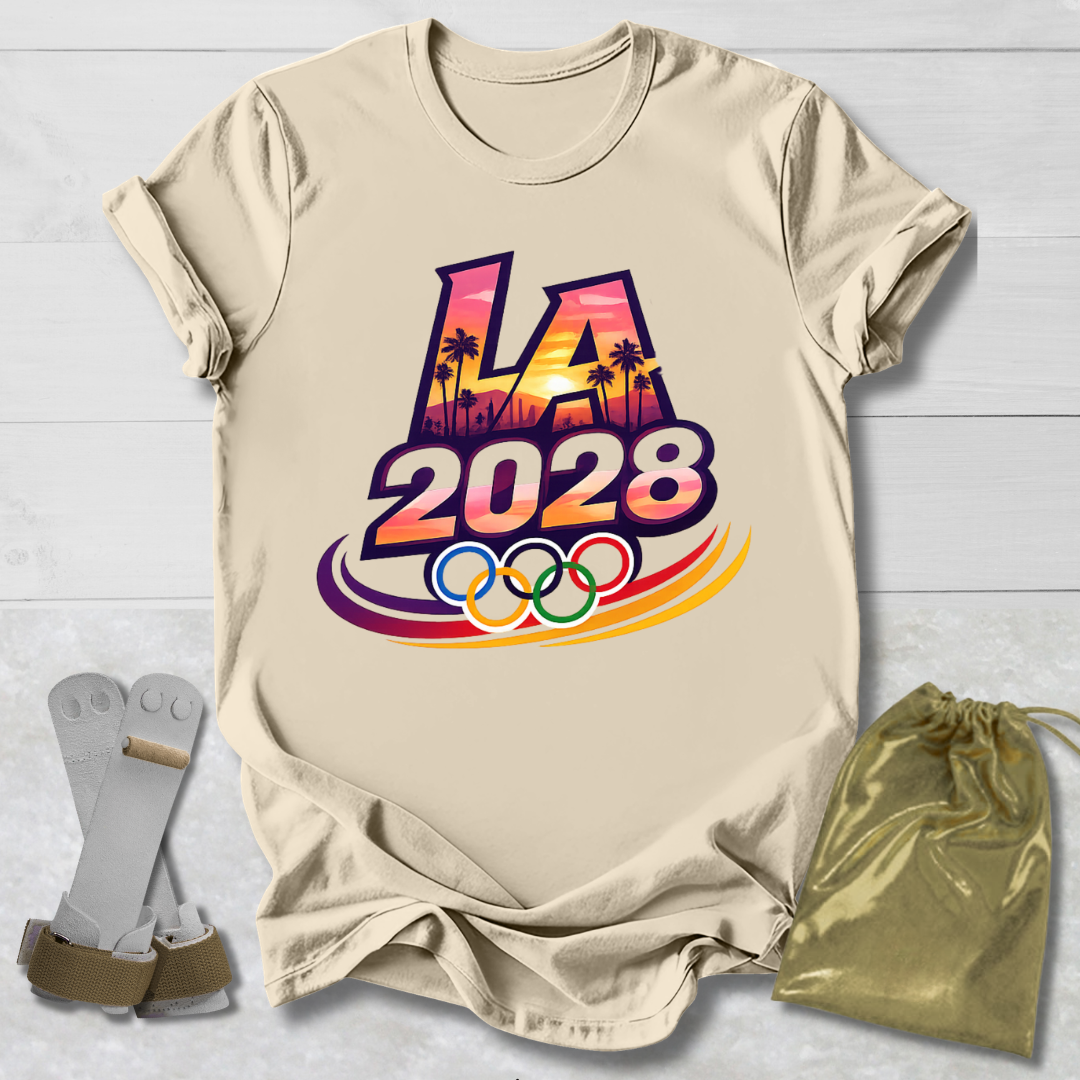 Beige t-shirt with 'LA 2028' Olympic design on a light wooden surface with socks and a drawstring bag.