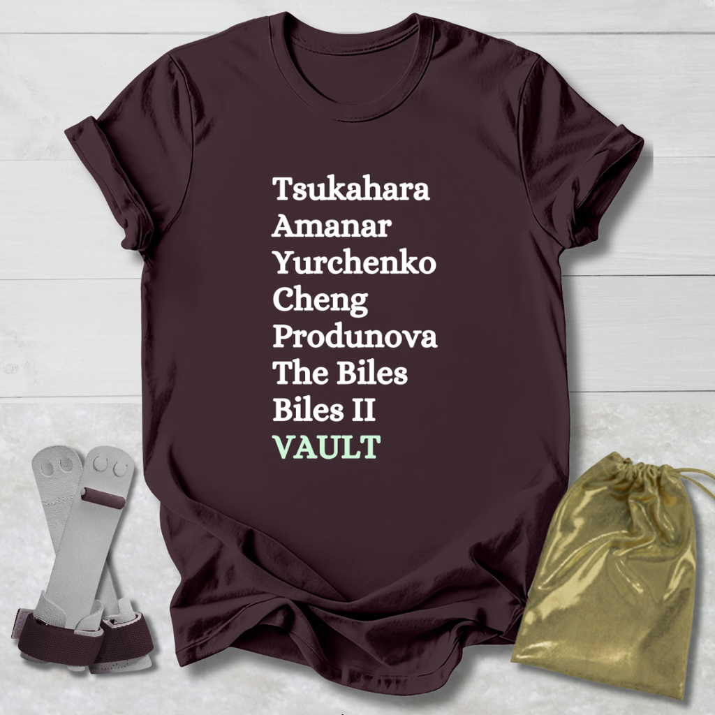 Maroon t-shirt with gymnast vault skills text on a light wooden surface with socks and a drawstring bag.