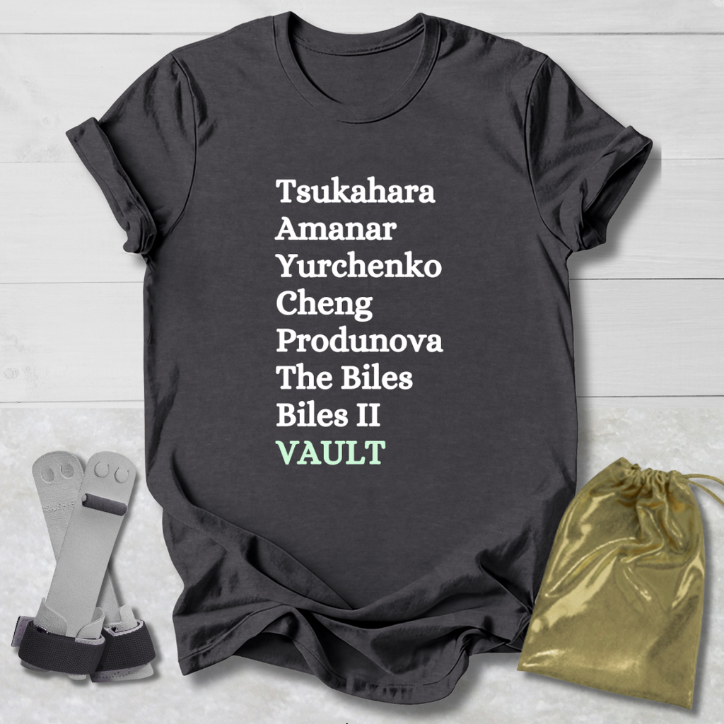 Dark gray t-shirt with white gymnast vault skills text on a light wooden surface with socks and a drawstring bag.