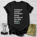 Black t-shirt with  gymnast vault skills text on a wooden surface with socks and a drawstring bag.