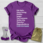 Purple t-shirt with gymnast uneven bars skills text, gray socks, and gold drawstring bag on a light wooden surface