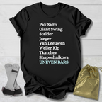 Black t-shirt with white gymnast uneven bars skills text on a wooden surface with socks and a drawstring bag.