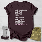 Maroon t-shirt with gymnast balance beam   moves text on a light wooden surface with socks and a drawstring bag.