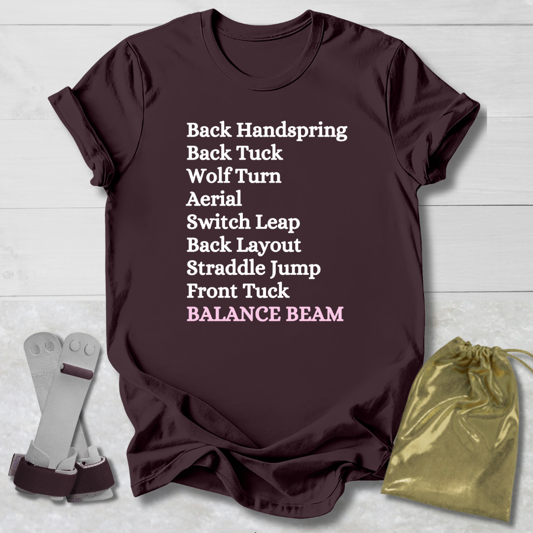 Maroon t-shirt with gymnast balance beam   moves text on a light wooden surface with socks and a drawstring bag.