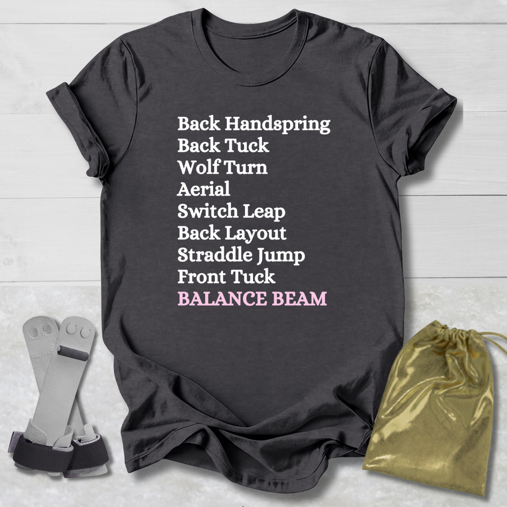 Dark gray t-shirt with balance beam gymnast moves text on a light wooden surface with socks and a drawstring bag.