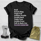Black t-shirt with white  gymnast floor exercise skills  text on a wooden surface with socks and a drawstring bag.