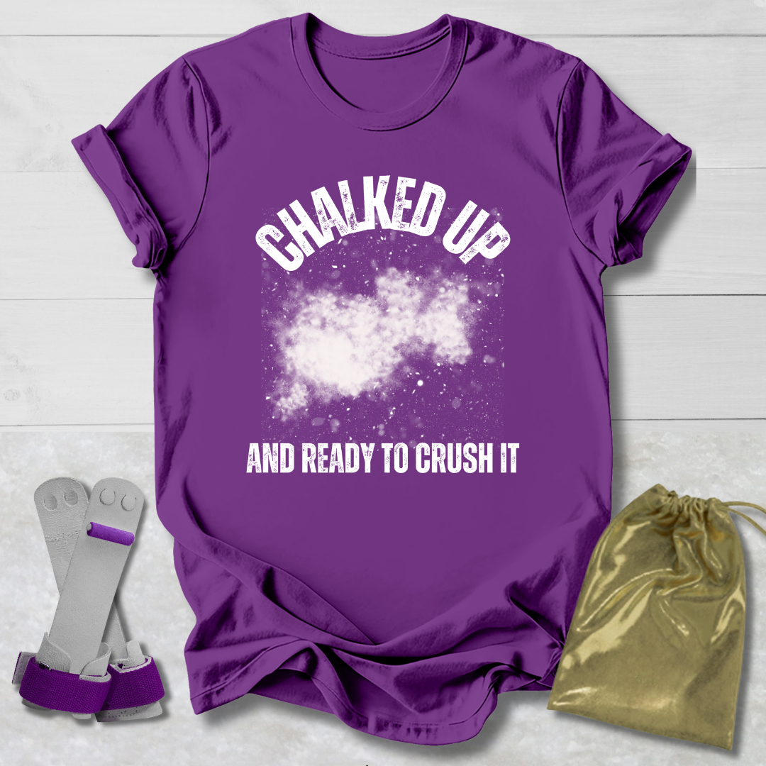 Purple t-shirt with 'Chalked Up and Ready to Crush It' text, socks, and drawstring bag on a light wooden surface.