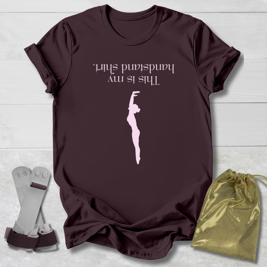 Maroon t-shirt with a graphic and  this is my handstand shirt text, socks, and a drawstring bag on a light wooden surface.