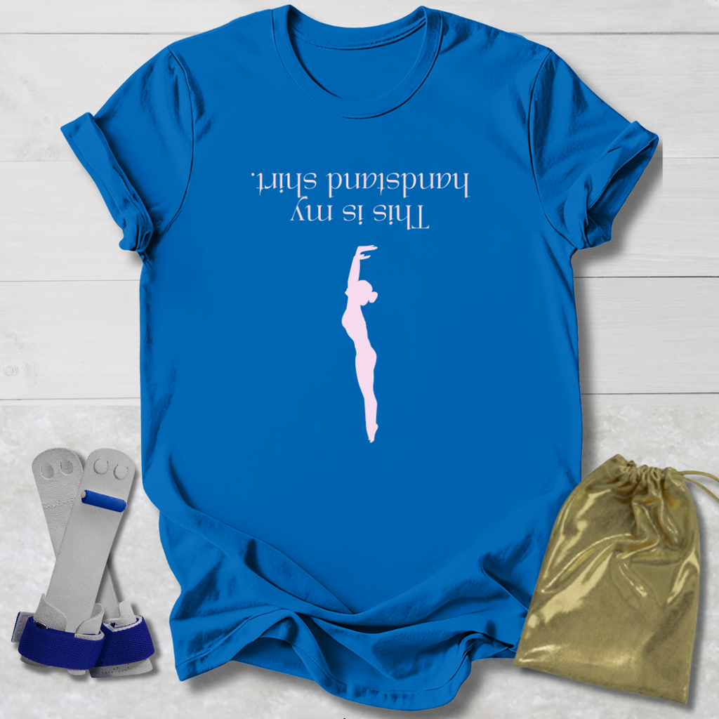 Blue t-shirt with a graphic and  this is my handstand shirt text, placed on a light wooden surface with socks and a drawstring bag.