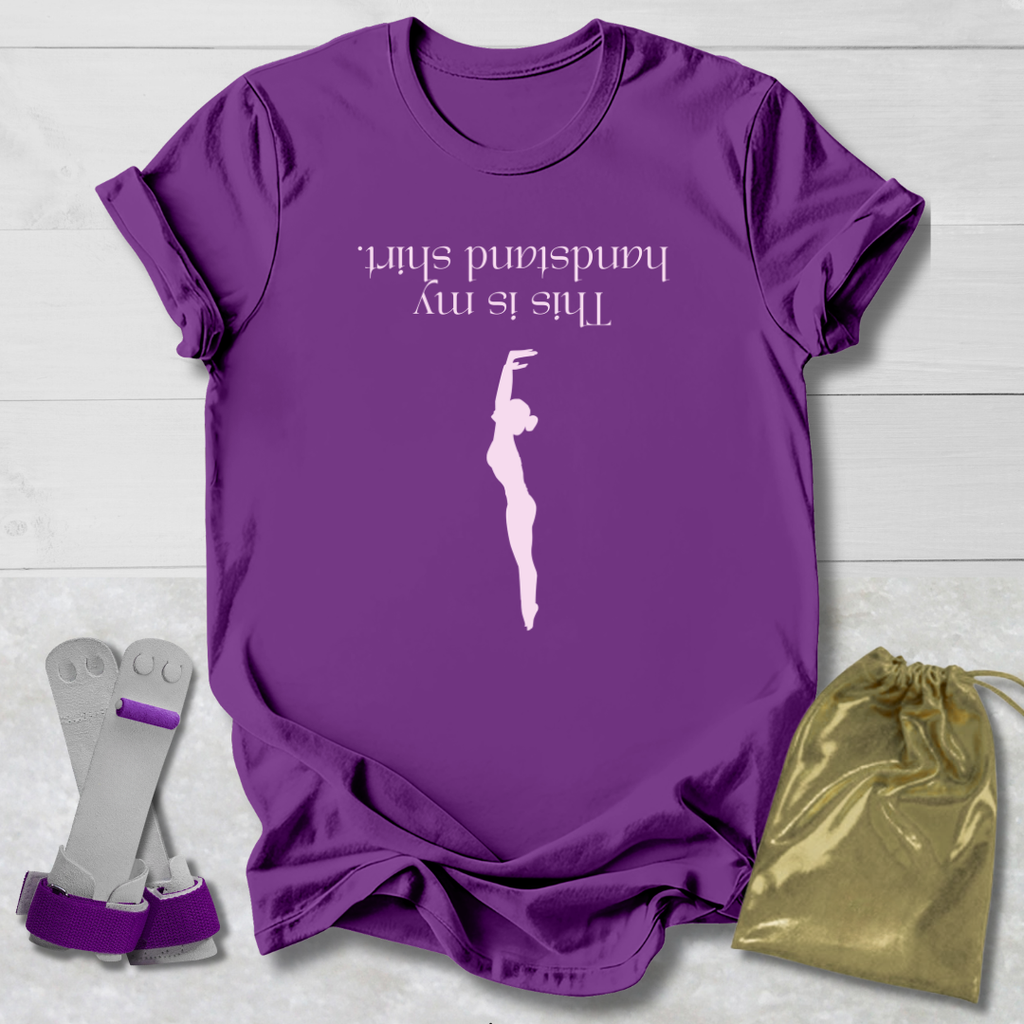 Purple t-shirt with a graphic and  this is my handstand shirt text, socks, and a drawstring bag on a light wooden surface.