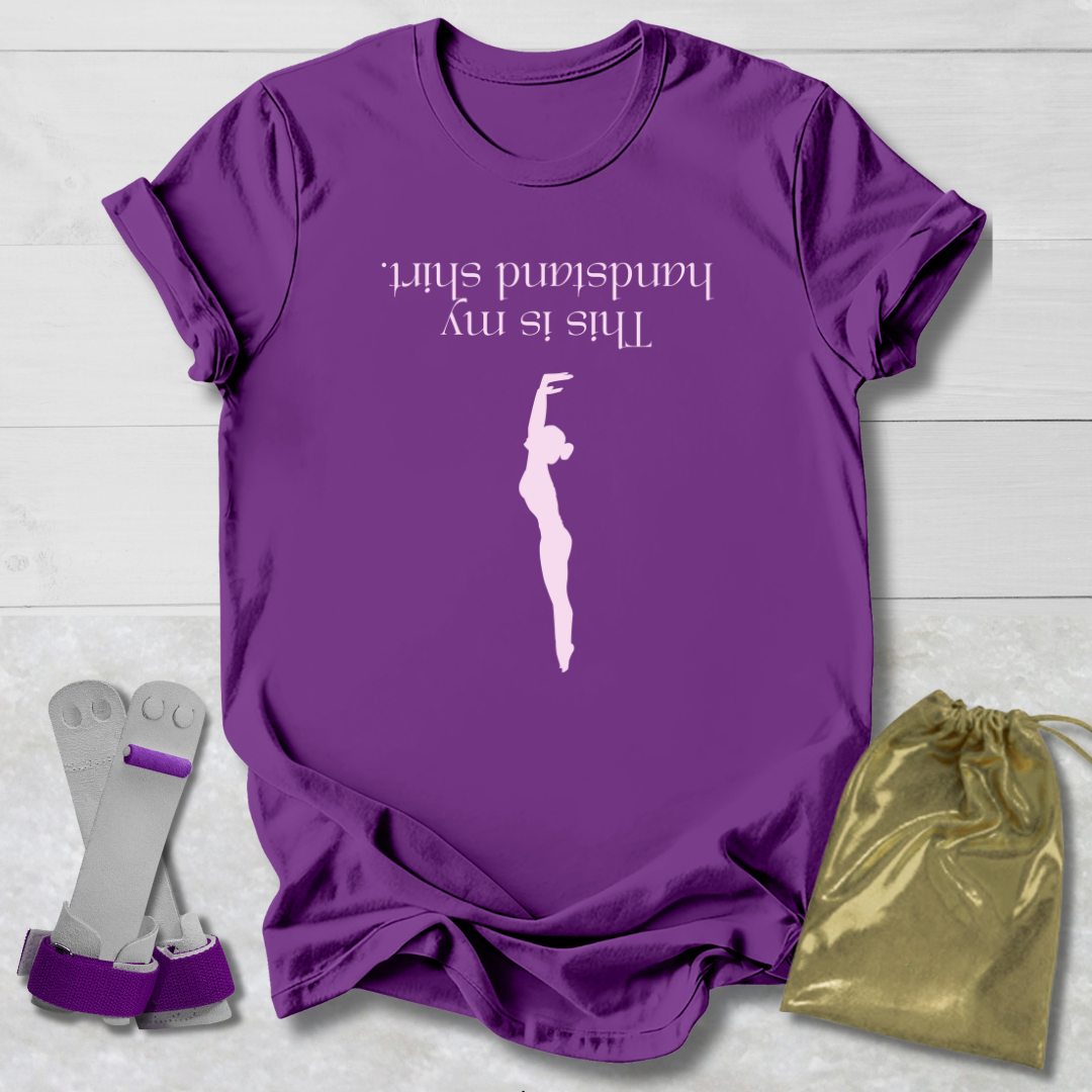 Purple t-shirt with a graphic and  this is my handstand shirt text, socks, and a drawstring bag on a light wooden surface.
