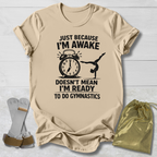 Beige t-shirt with a graphic and gymnast text on a light wooden surface, accompanied by socks and a drawstring bag.