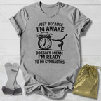 Gray t-shirt with gymnastics-themed text and graphics on a wooden surface with socks and a drawstring bag.