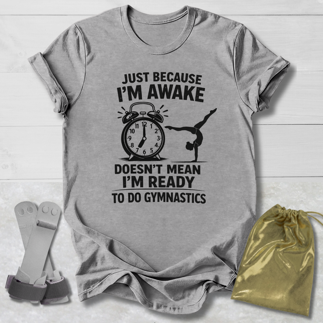 Gray t-shirt with gymnastics-themed text and graphics on a wooden surface with socks and a drawstring bag.