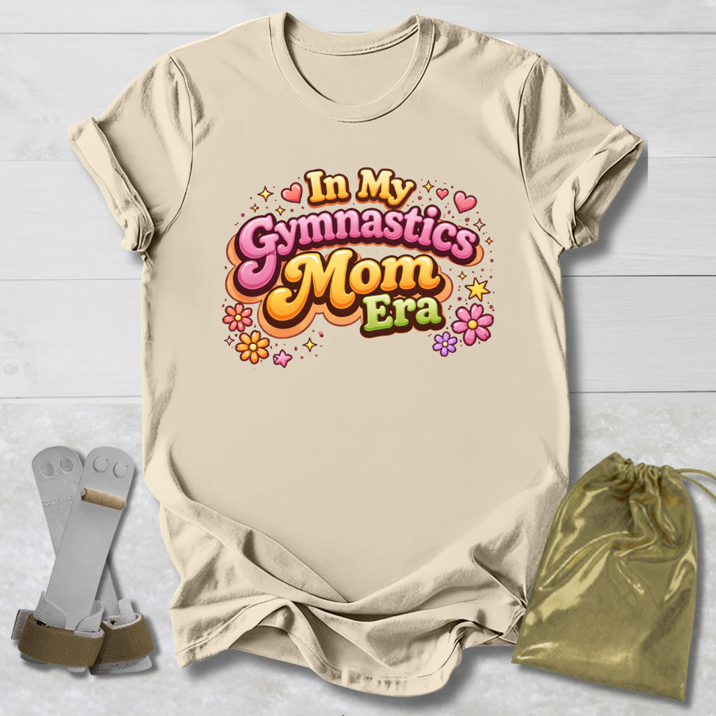 Beige t-shirt with 'In My Gymnastics Mom Era' text, socks, and drawstring bag on a light wooden surface.