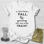 White t-shirt with humorous gymnast if you didn't fall, did you even train? text design on a light wooden surface with socks and a drawstring bag.