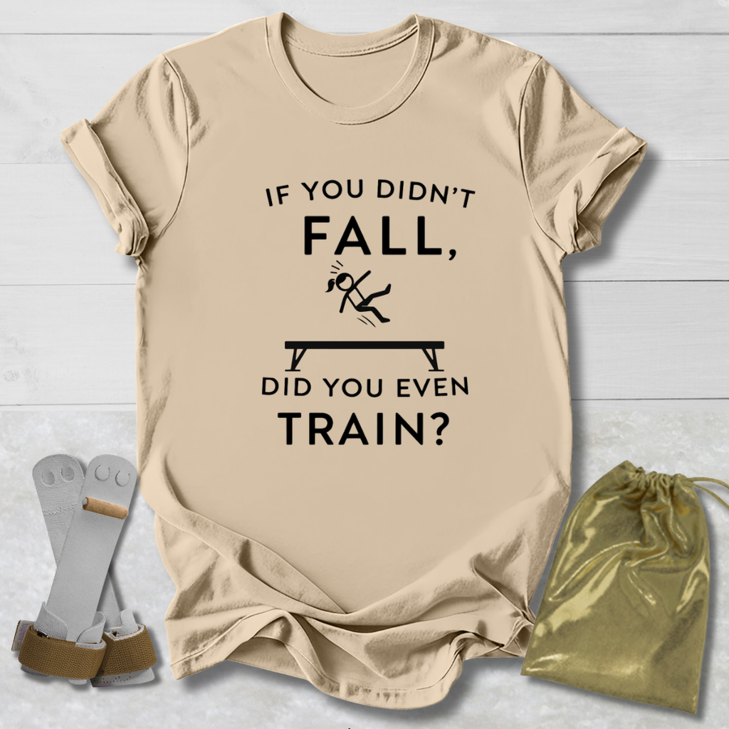 Beige t-shirt with humorous gymnast if you didn't fall, did you even train? text design on a light wooden surface with socks and a drawstring bag.