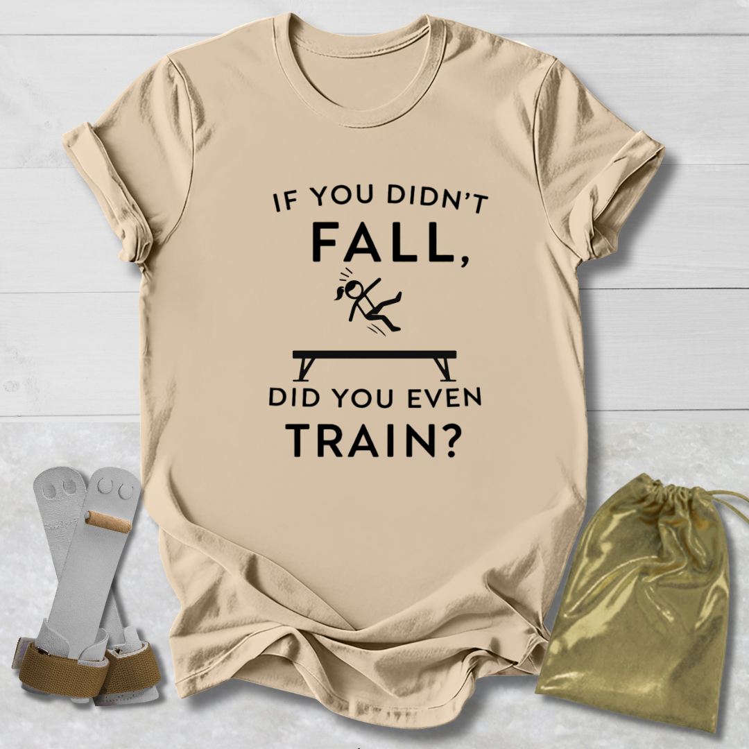 Beige t-shirt with humorous gymnast if you didn't fall, did you even train? text design on a light wooden surface with socks and a drawstring bag.