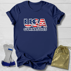 Navy blue t-shirt with 'USA Gymnastics' design on a light wooden surface, with socks and a drawstring bag in the foreground.