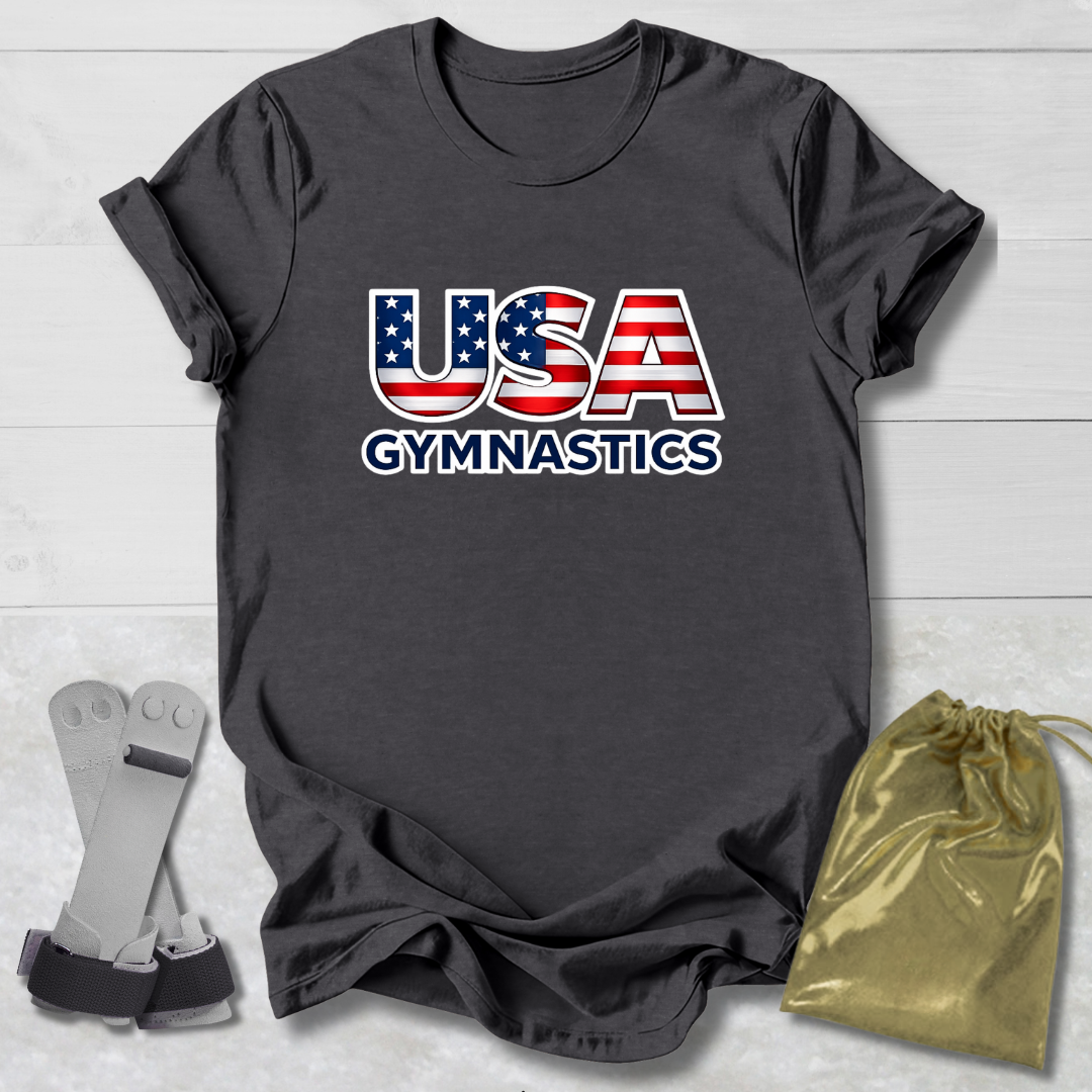 Gray t-shirt with 'USA Gymnastics' design on a light wooden surface, with socks and a drawstring bag in the foreground.