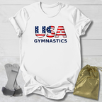 White t-shirt with 'USA Gymnastics' text and American flag design on a light wooden surface.