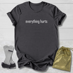 Dark gray t-shirt with 'everything hurts' text, socks, and drawstring bag on a light wooden surface