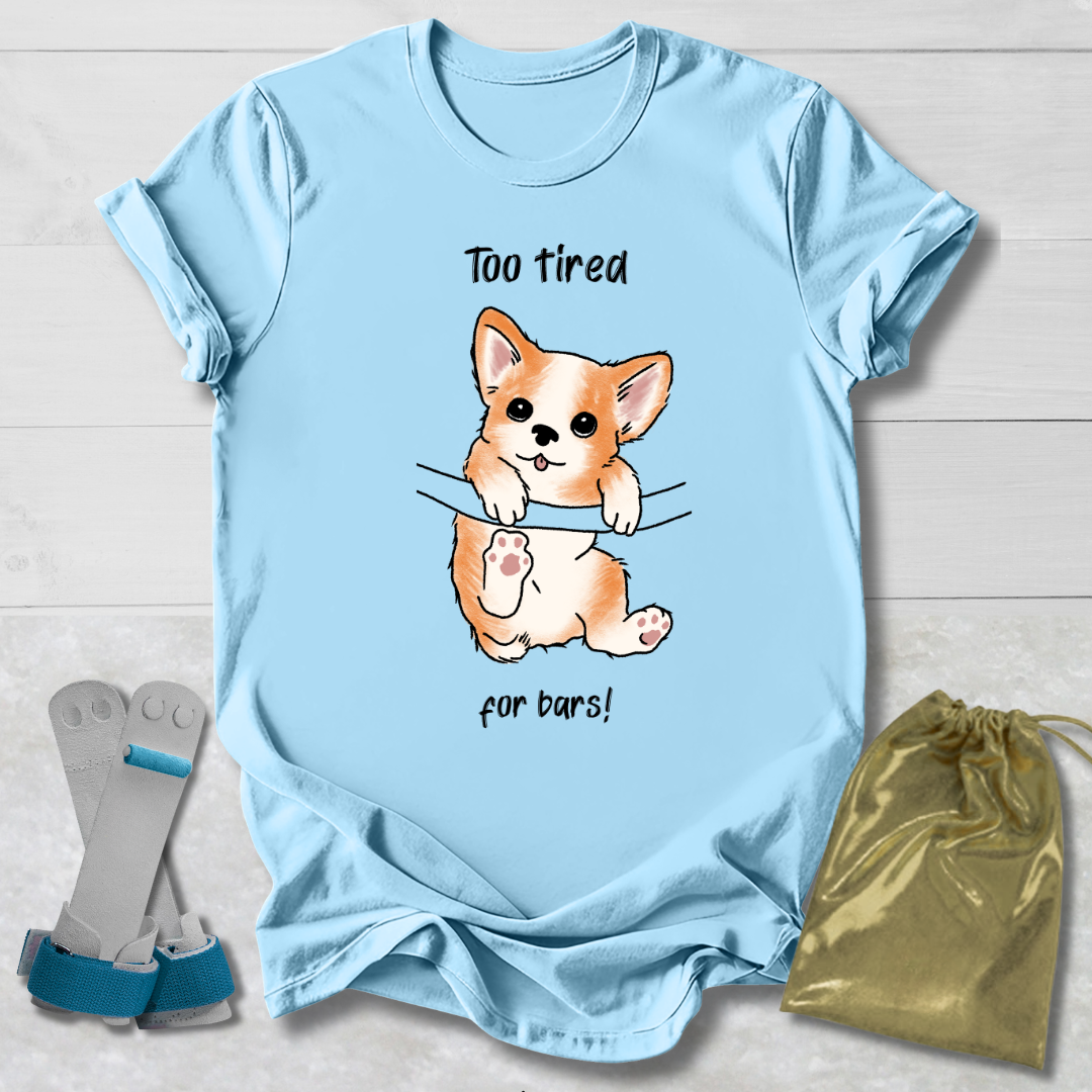 Light blue t-shirt with a cartoon dog graphic and  too tired for bars gymnast text, displayed with socks and a drawstring bag on a light wooden surface.