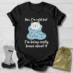 Black t-shirt with a cat Yes I'm cold graphic and text on a wooden surface, accompanied by socks and a drawstring bag.